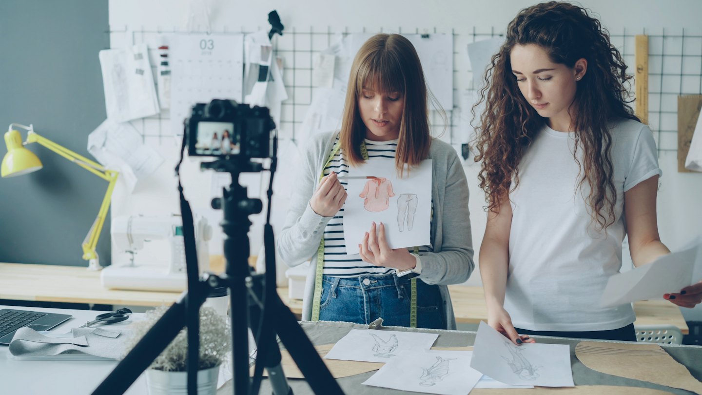 Zwei Designerinnen arbeiten in einem hellen Atelier an Modezeichnungen.